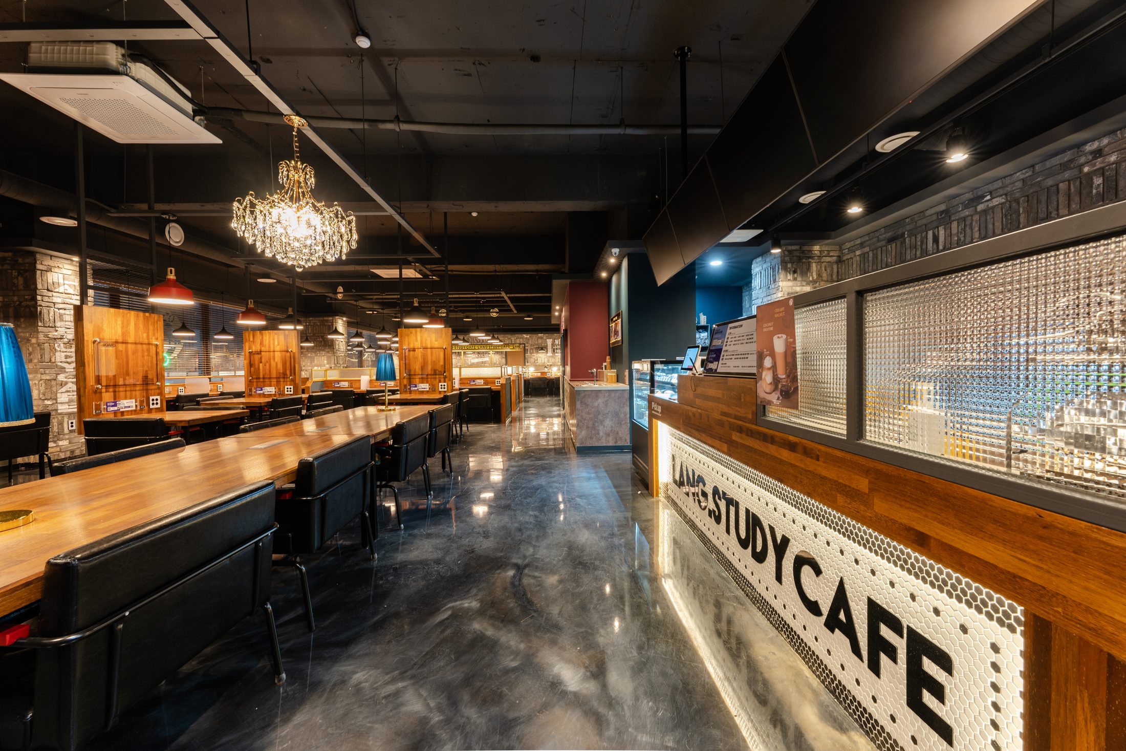 샹들리에 아래 나무색 긴 책상과 LANG STUDY CAFE 카운터가 놓인 스터디카페 내부