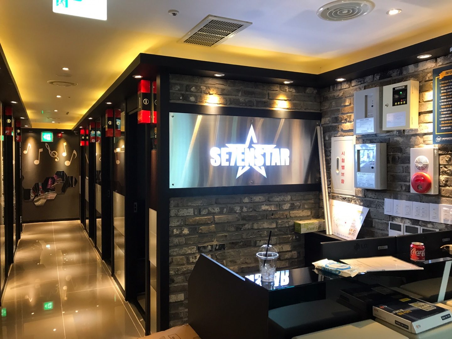 벽돌무늬 벽에 SEVENSTAR 조명 간판이 걸린 코인노래방 카운터와 양쪽 복도